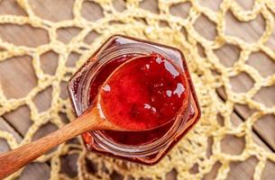 Wooden spoon full of  strawberry jam on yellow knitted napkin on wooden table. photo