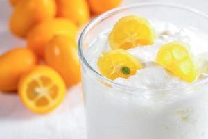 Close-up part of glass cup with yogurt with slices of kumquat on whole fruits background. photo