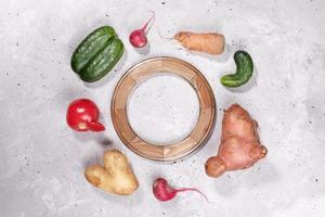 Set of ripe ugly vegetables laid around of rounded wooden frame on grey concrete background. photo