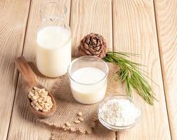 Healthy cedar products milk in glass and bottle, flour, nuts on burlap napkin on wooden table. photo