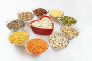 Round glass bowls with superfood are standing around red heart-shaped bowl on white background. photo