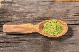 Wooden spoon with japanese green matcha tea powder on old wooden board. Top view. photo
