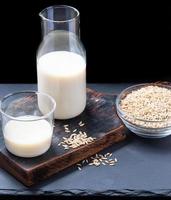 Vegan dairy free oat milk in glass bottle and glass and oat seeds on glass bowl on dark background. photo