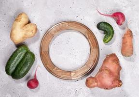 Set of ripe ugly vegetables and round wooden frame on grey concrete background. photo