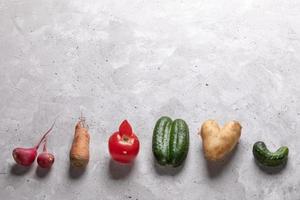 Ugly vegetables laid out in row on grey concrete background. photo