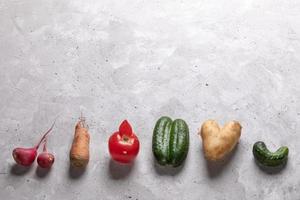 verduras feas dispuestas en fila sobre fondo de hormigón gris. foto