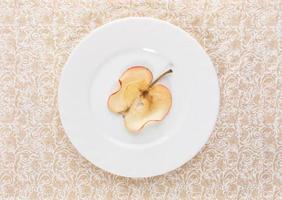 One slice of dried apple on white plate on beige ornate patterned background. photo