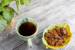 Ceramic cup of healing beverage of birch mushroom chaga and shaped bowl with chaga pieces on light wooden backdrop. photo