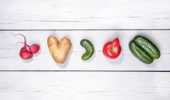 conjunto de cinco verduras feas patata, tomate, pepino y rábano dispuestos en fila sobre fondo blanco de madera. foto