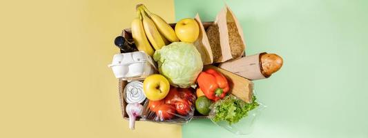 Top view of cardboard box with food products on color green-yellow background. Safe delivery. Banner with copy space. photo