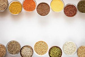 Top view to glass bowls with cereals, beans and seeds on white background with copy space in middle. photo