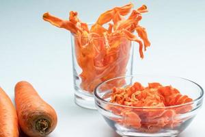 Transparent bowl and glass with orange carrot chips and whole carrots on gentle blue background. photo