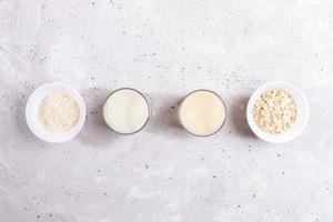 Glasses with rice and oat milk, bowls with rice seeds and oat flakes laid out in row on concrete background. photo