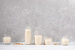 Set of glass containers with oat milk on white wooden table on concrete wall background. photo