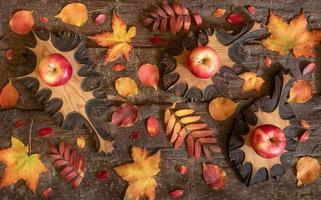 Autumn composition of colorful natural leaves and wooden carved leaves with apples on them on tree bark background. photo
