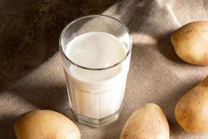 Glass of drink from potato, potato tubers on burlap. Non dairy alternative milk. Selective focus. photo