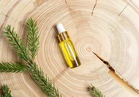 Small glass bottle with coniferous spa aromatic essential spruce oil and branch on wooden saw cut with copy space. photo