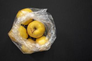 Yellow ripe apples in opened plastic bag on grey background. photo