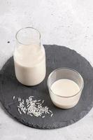 Close-up drinking glass and glass bottle with  rice milk on round shale board on light background. photo