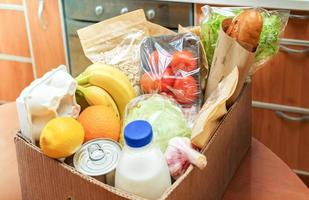 caja de cartón de primer plano con diferentes productos alimenticios frescos envasados en la mesa de la cocina. entrega segura. enfoque selectivo. foto