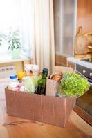 Cardboard box with fresh packed food products on wooden table in kitchen interior. Safe delivery. Selective focus. photo