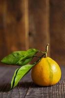 One yellow mandarin with leaves is lying on wooden table on wooden background. photo