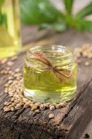 Hemp oil in glass jar and grains of cannabis on old wooden board, bottle with oil and leaves are blurred. photo