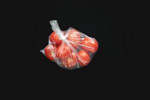 Red ripe tomatoes in closed plastic bag in center of black background. photo