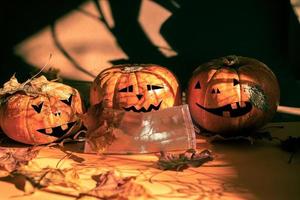 tres calabazas de halloween pintadas como linterna de jack, una con máscara protectora, hojas de otoño, sombras mágicas. nueva normalidad. foto