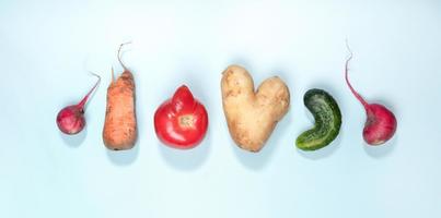 seis verduras feas maduras patata, tomate, pepino y rábano dispuestos en fila sobre fondo azul claro. foto