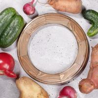 Close-up round wooden frame and ugly vegetables laid around it on grey concrete background. photo