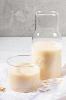 Close-up glass of dairy free oat milk and flakes on white napkin on concrete background. photo