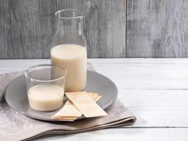 Dairy free oat milk in glass bottle and glass on white table on grey wooden background. photo