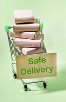 Stack of packed boxes in mini shopping trolley with label Safe Delivery. Light green backdrop. Vertical orientation. photo