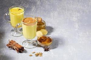 Turmeric milk for immunity. Two glasses for mulled wine with golden milk with ingredients on light grey background. photo