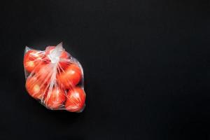 tomates rojos en una bolsa de plástico cerrada sobre fondo negro. foto