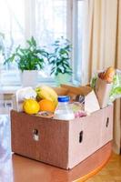 Cardboard box with food products on wooden kitchen table in interior. Safe delivery concept. Food donation. photo