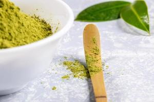 Close-up special wooden bamboo spoon with green matcha tea powder, white bowl with tea powder and fresh leaves on grey. photo