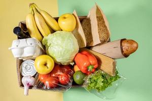 Top view of cardboard box with fresh food products on green-yellow background. Safe delivery. Top view. photo