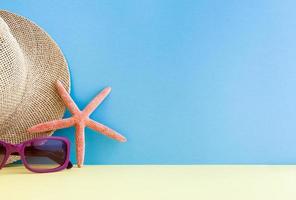Lilac sunglasses, straw hat and starfish lying on the yellow surface on a blue background. photo
