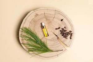 Small glass bottle with coniferous spa aromatic essential cedar oil, branch, nuts on wooden saw cut on beige backdrop. photo