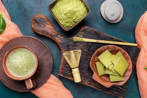 Green matcha tea and powder in brown ceramic cups and matcha chocolate on wooden serving board on emerald background. photo