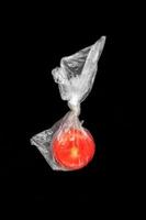 One red ripe tomato in closed plastic bag in center of black background. photo