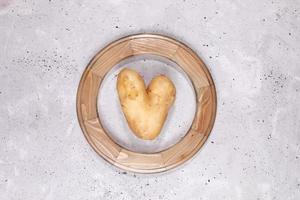 One ugly heart shaped potato inside of round woodem frame in center of grey concrete background.