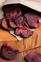 Close-up beetroot chips fall out of paper bag on wooden cut. photo