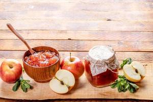 cuenco de madera y tarro de cristal con mermelada de manzana y manzanas y menta verde sobre tabla de madera sobre mesa de madera antigua. foto