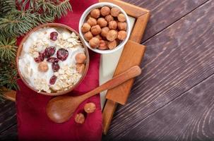 Wooden and ceramic bowls of yogurt and hazelnuts on red napkin on tray on wooden table. photo