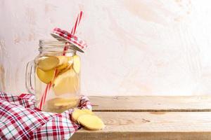 Glass jar with ginger water with drinking straw and tartan cap and cloth on wooden planks on light background. photo