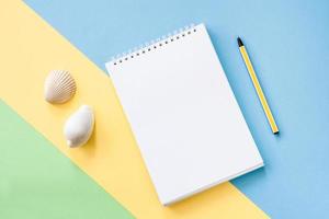 Summer vacations concept with yellow stripe and pen, notepad and seashells on blue-green background. photo