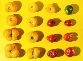 Rhythm pattern of different color farm tomatoes with hard shadows on bright yellow background. photo